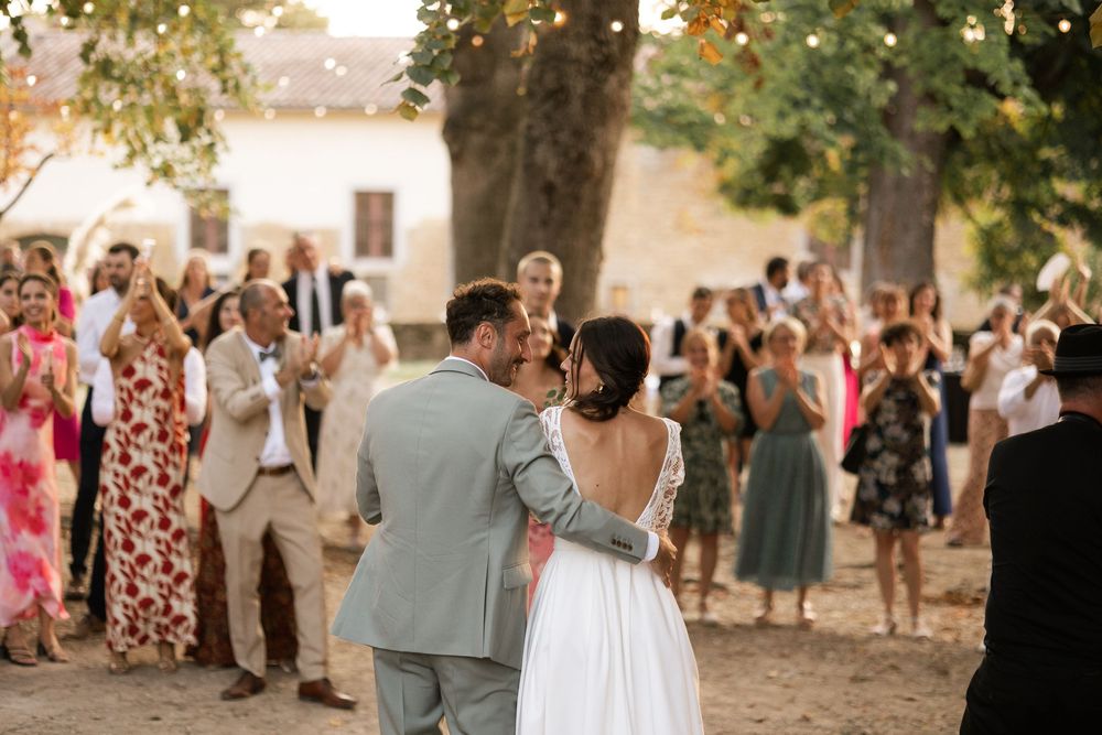 Outdoor wedding reception under trees with guests mingling during golden hour.