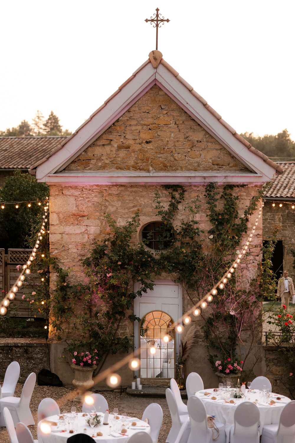 Outdoor wedding reception setup with string lights at stone chapel venue.