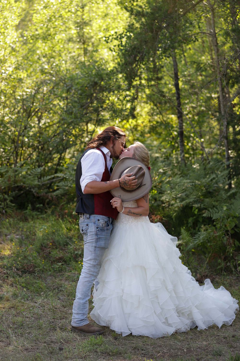 Romantic wedding couple shares intimate moments in a wooded outdoor setting with natural sunlight filtering through trees.