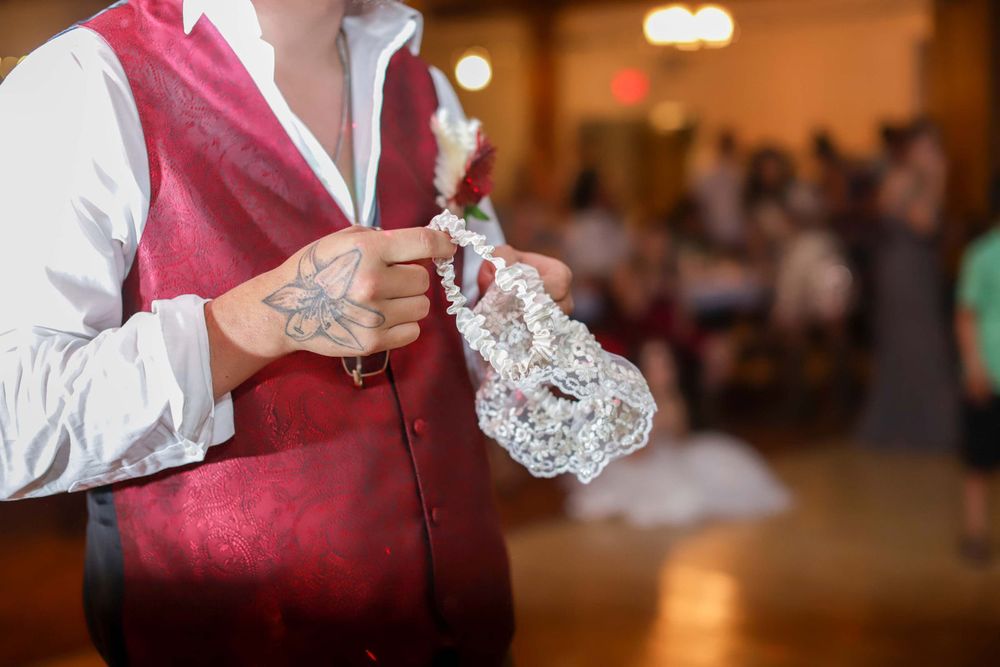 A person in a burgundy vest serves food at a catered event with warm lighting and blurred background details.