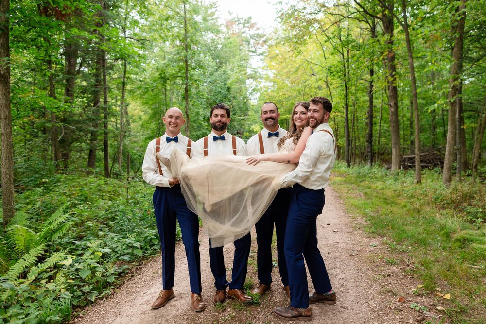 Group of people in light colored attire walking along a scenic wooded trail through lush green forest.