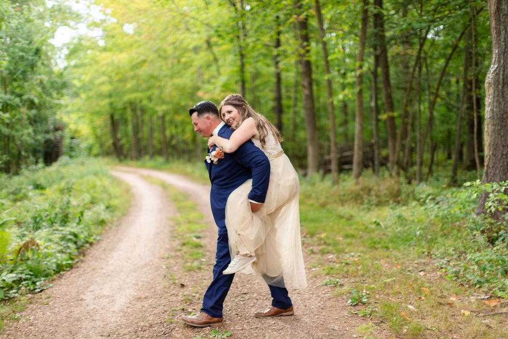 A romantic couple embraces on a winding dirt path through a lush green forest during a summer engagement photoshoot.