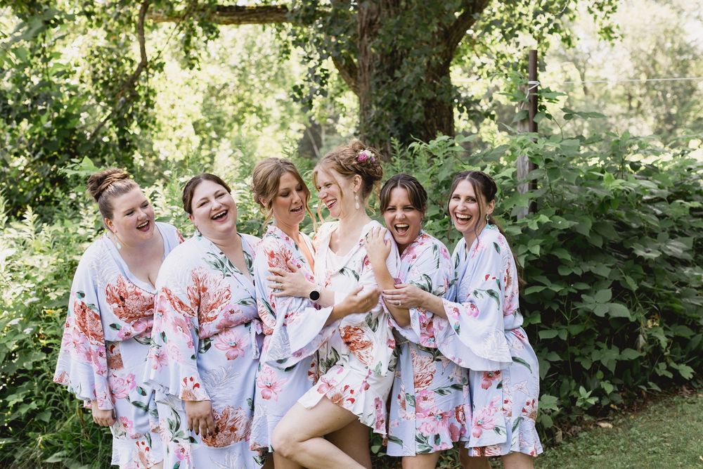 Bridesmaids in floral robes gather together laughing and celebrating before the wedding ceremony.