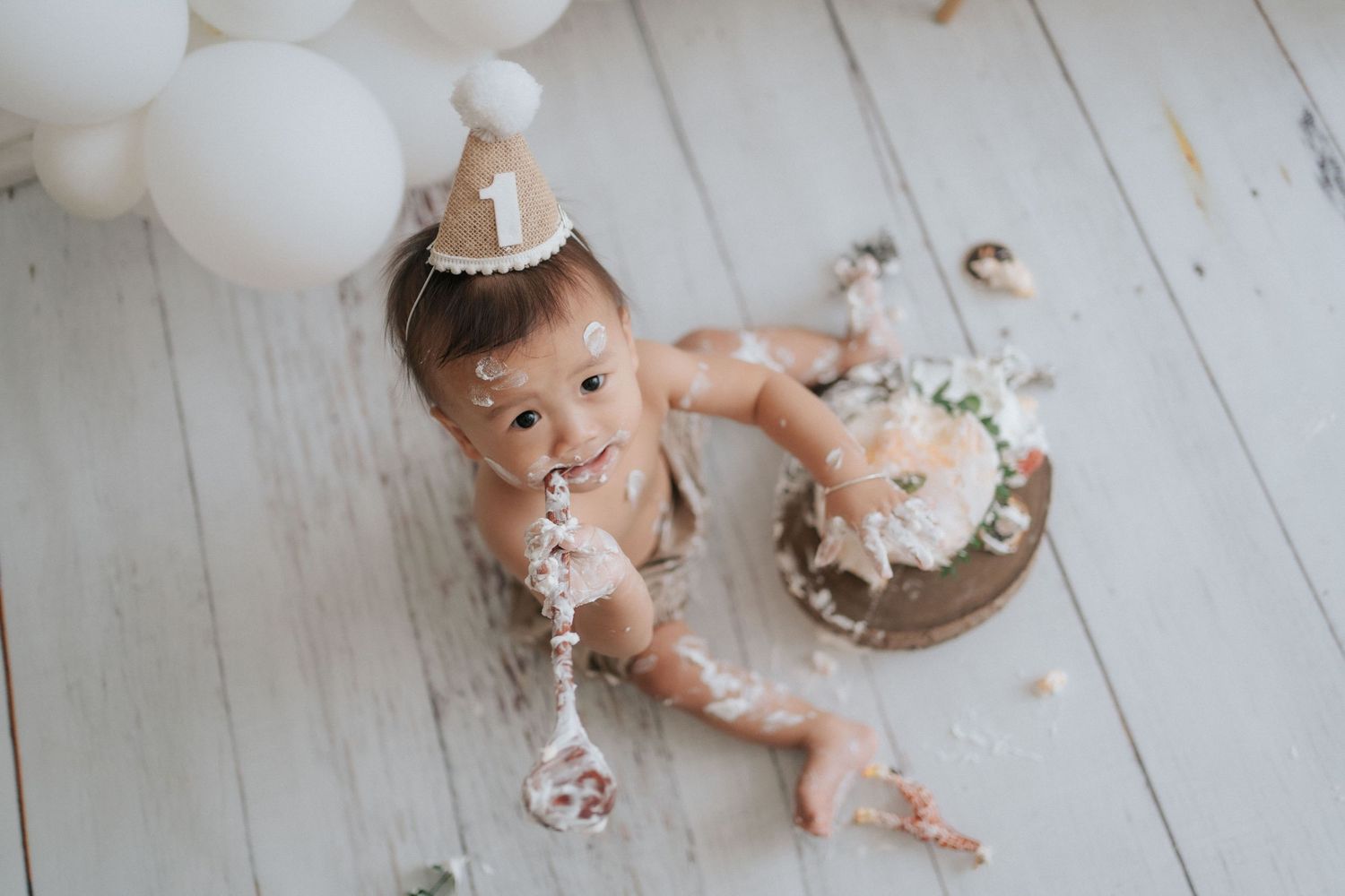 Baby smashes cake and gets messy while celebrating their first birthday during a cake smash photo session.