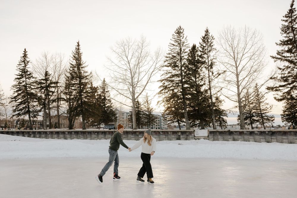 Two people ice skating together on a frozen pond surrounded by evergreen trees in winter.