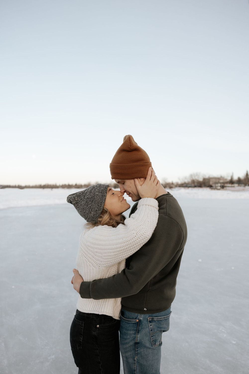 A couple embraces in a snowy winter landscape wearing warm clothing.