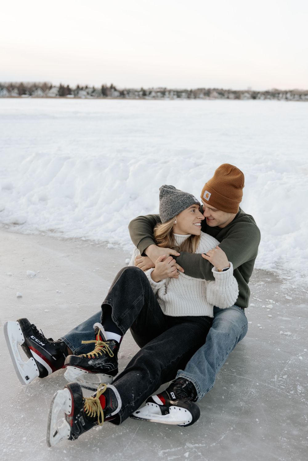 A couple in winter clothing shares tender moments while sitting on a frozen lake in a romantic winter photoshoot.