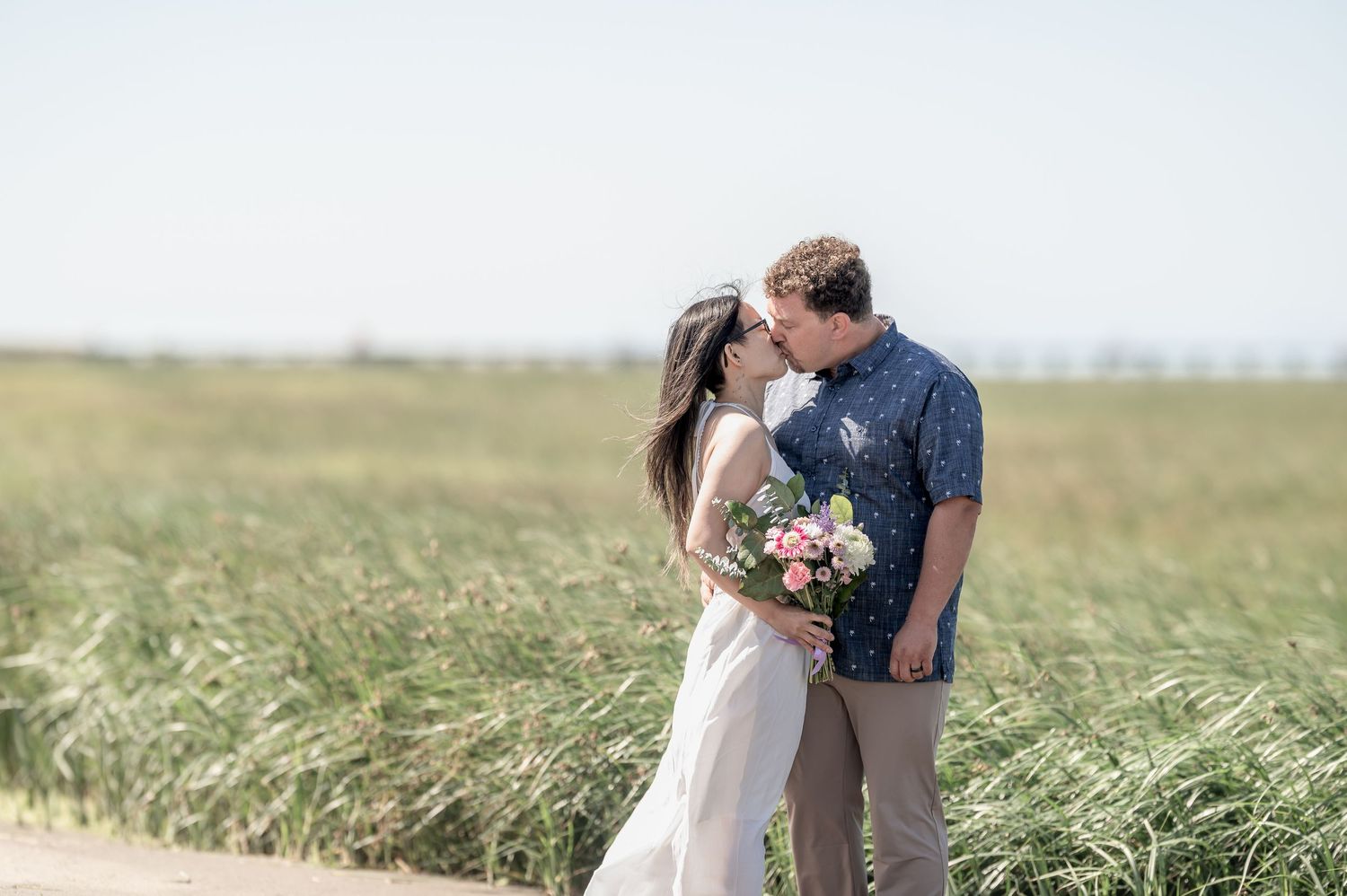 A romantic couple embraces in a scenic field of tall grass swaying in the breeze during golden hour.
