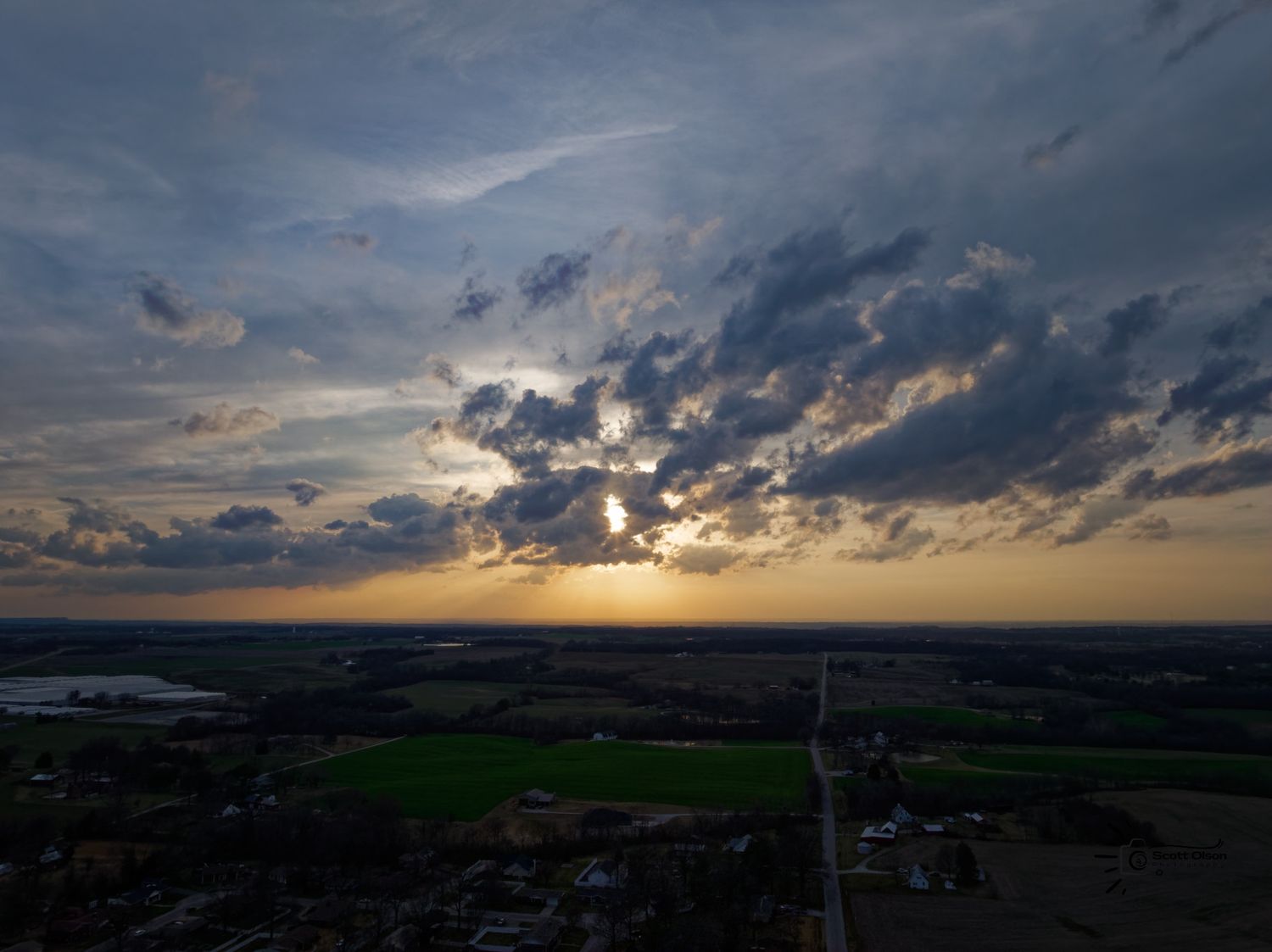 Dramatic sunset sky with sunbeams breaking through clouds over rural landscape.