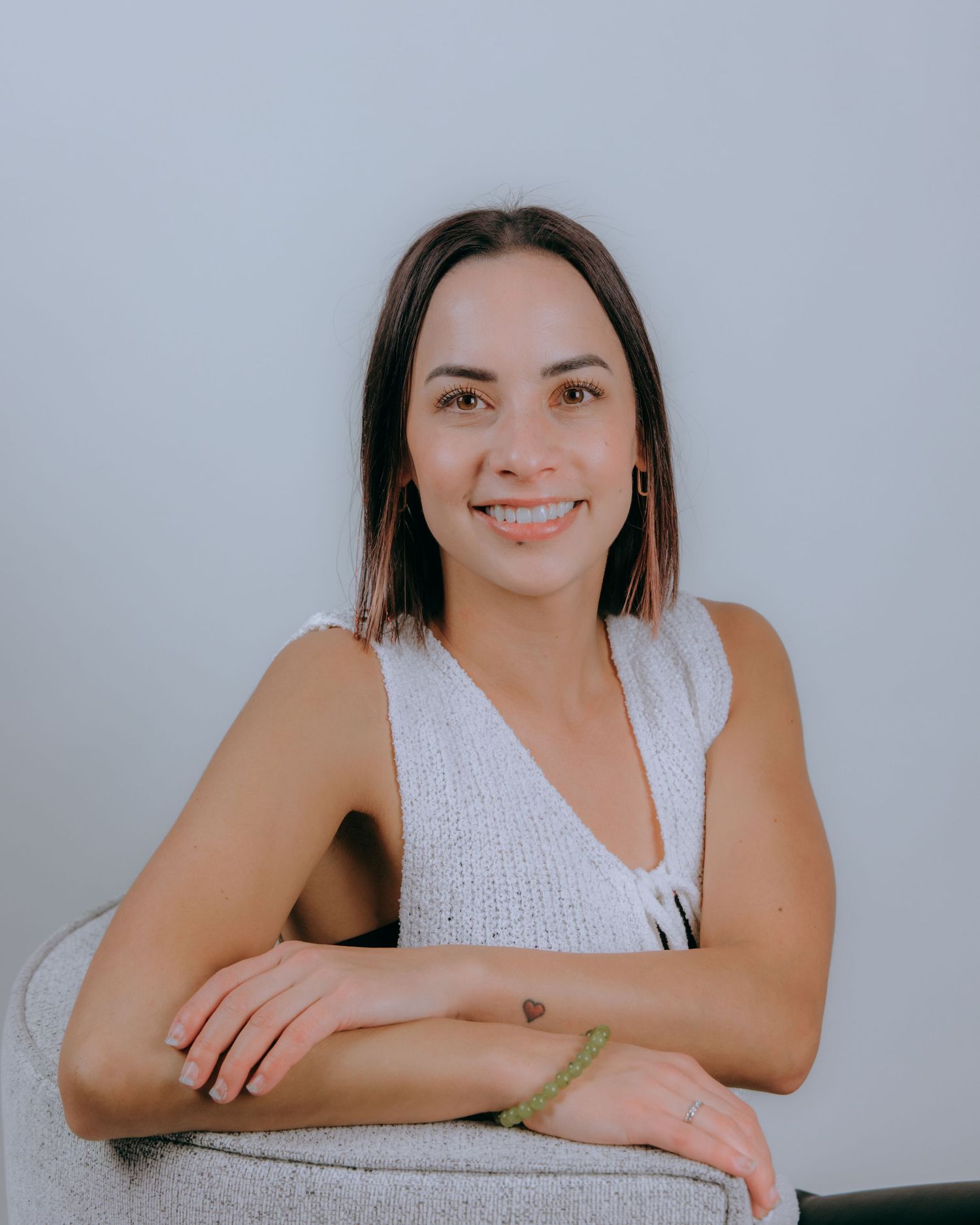 Person in white sleeveless top posing against light background for casual portraits.