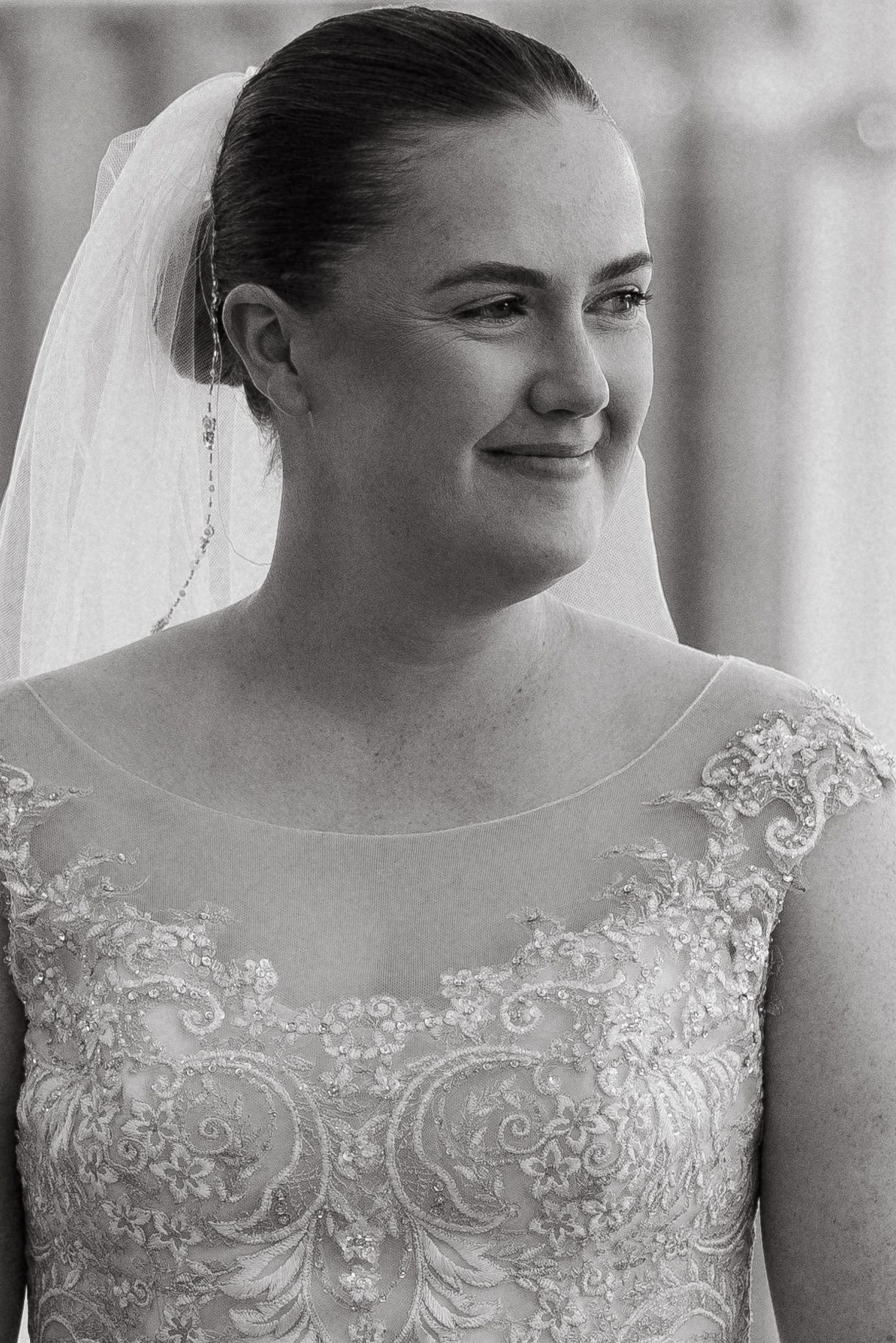 Black and white portrait of a radiant bride wearing an elegant lace gown and veil.