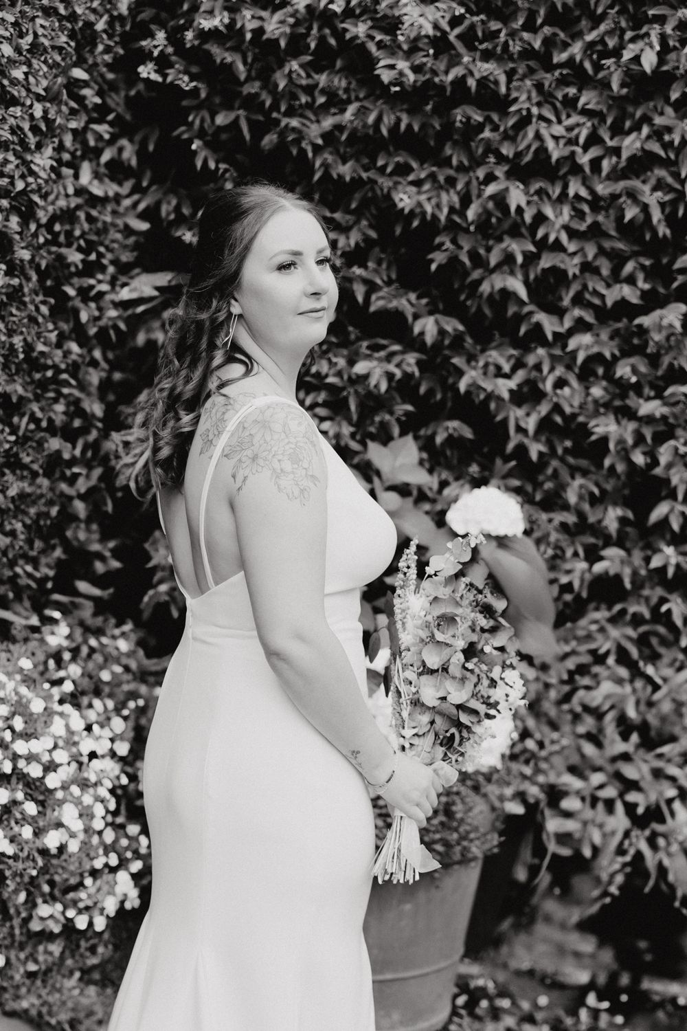 A bride in a fitted white wedding dress poses in front of an ivy-covered wall, captured by Apertured Media Auckland Wedding Photographer.