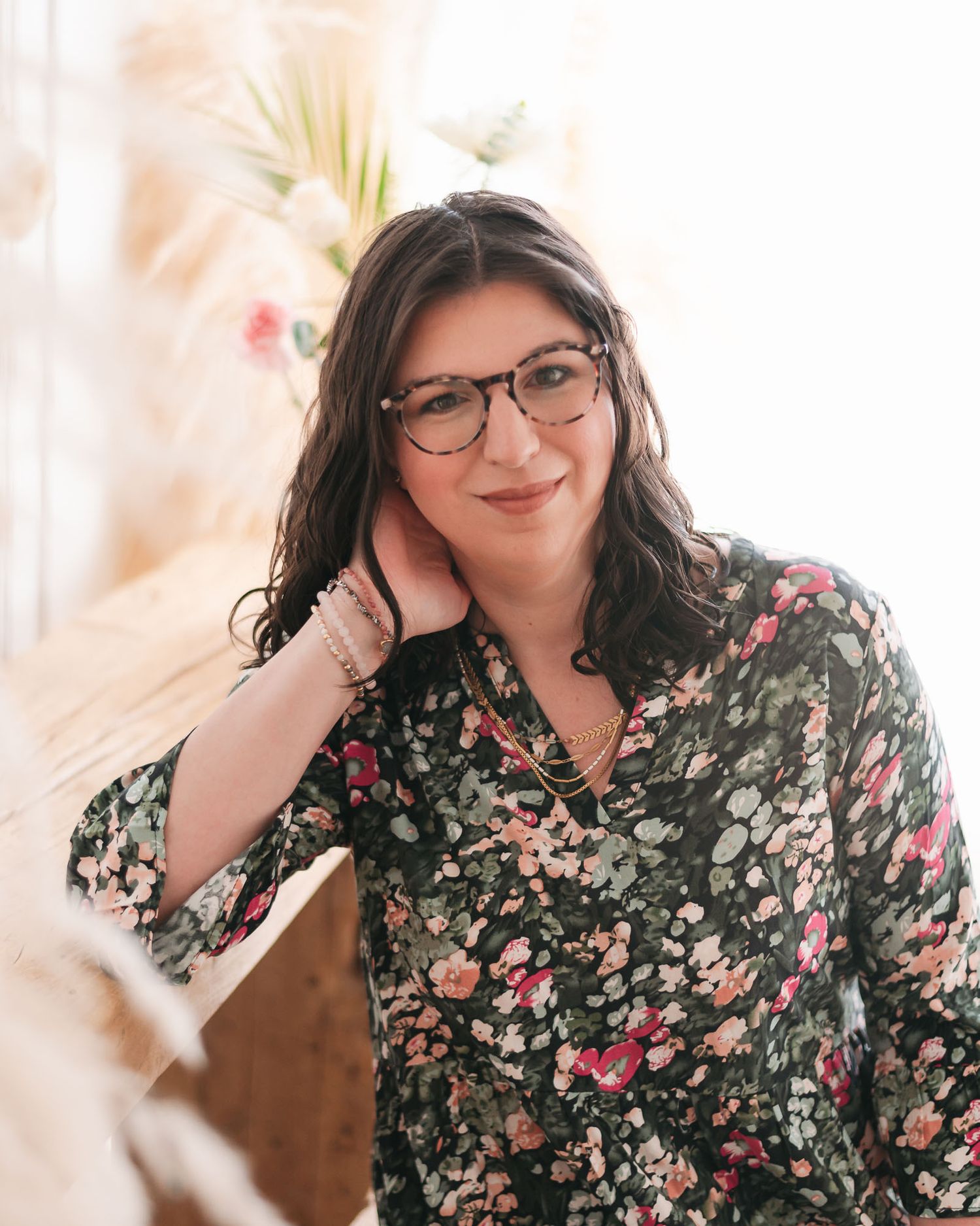 Portrait of someone wearing glasses and a green floral print blouse while posing against a soft light background.