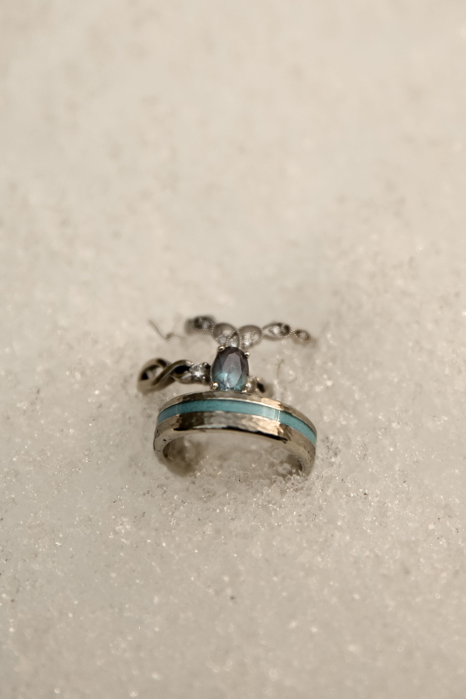 Close-up of a turquoise and silver ring with gemstone accents on sparkly surface.