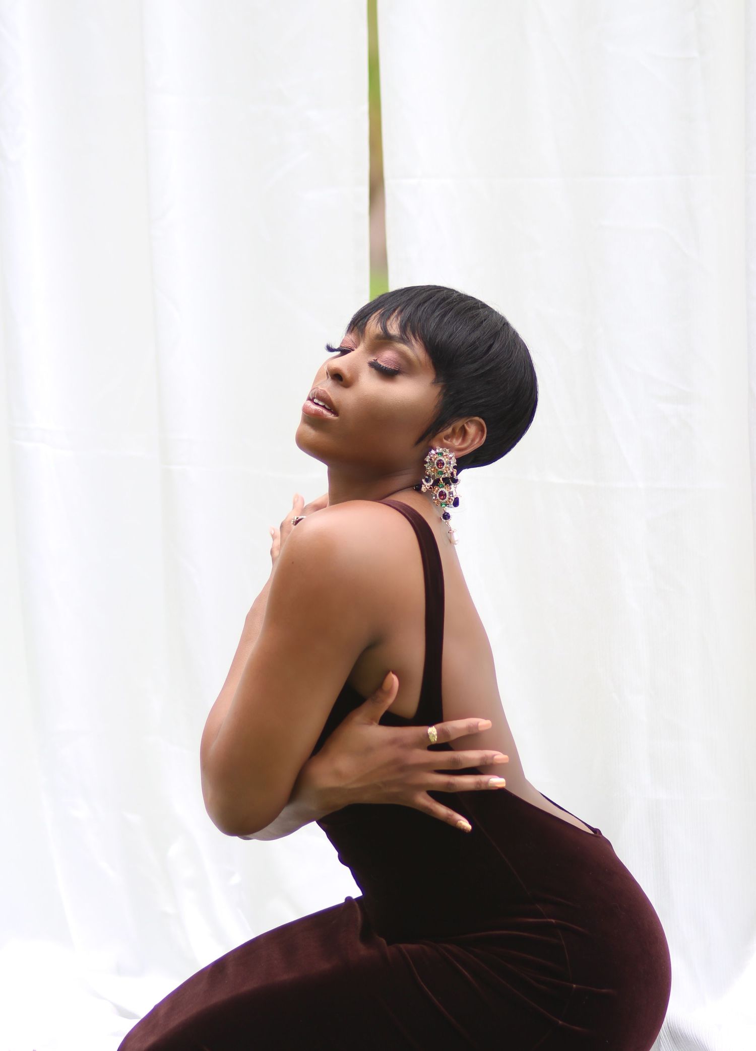 Artistic portrait in profile pose wearing statement earrings against white backdrop.