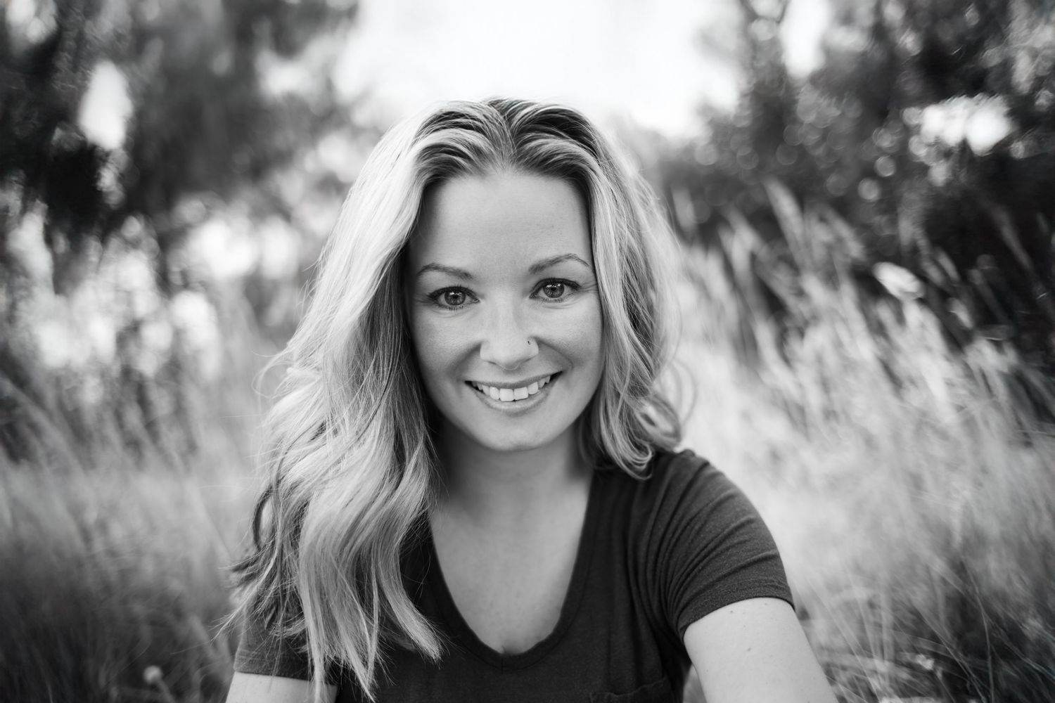 Portrait of someone with blonde hair smiling outdoors in a black shirt.