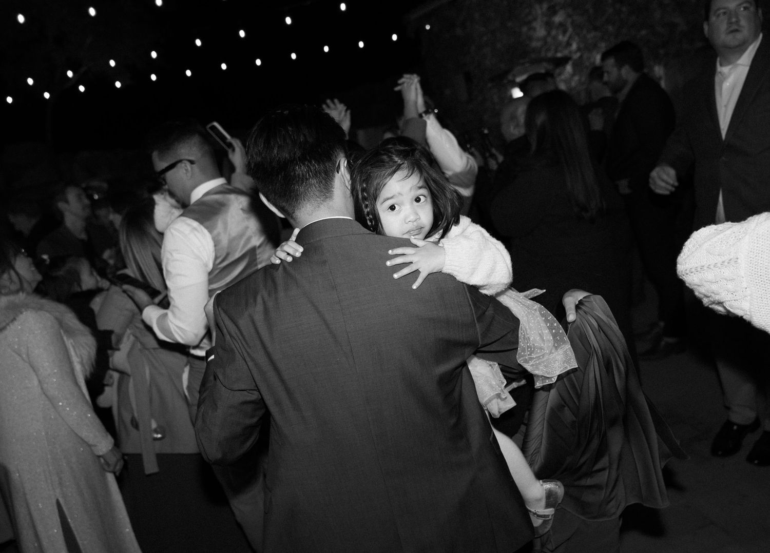 People dancing in a dimly lit ballroom with string lights overhead in a vintage black and white photograph.