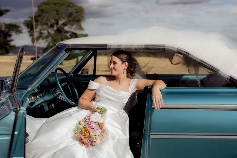 Classic blue vintage car serves as stylish wedding transportation with bride's bouquet visible.