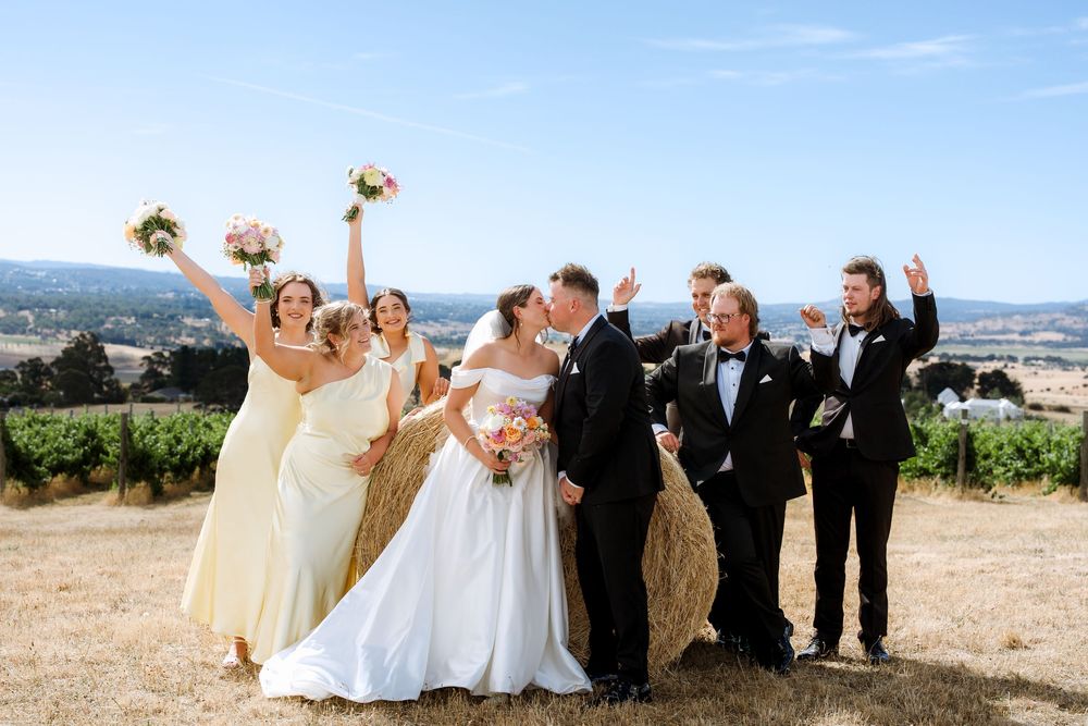 Wedding party poses in a series of candid celebratory shots against a scenic vineyard and mountain backdrop.