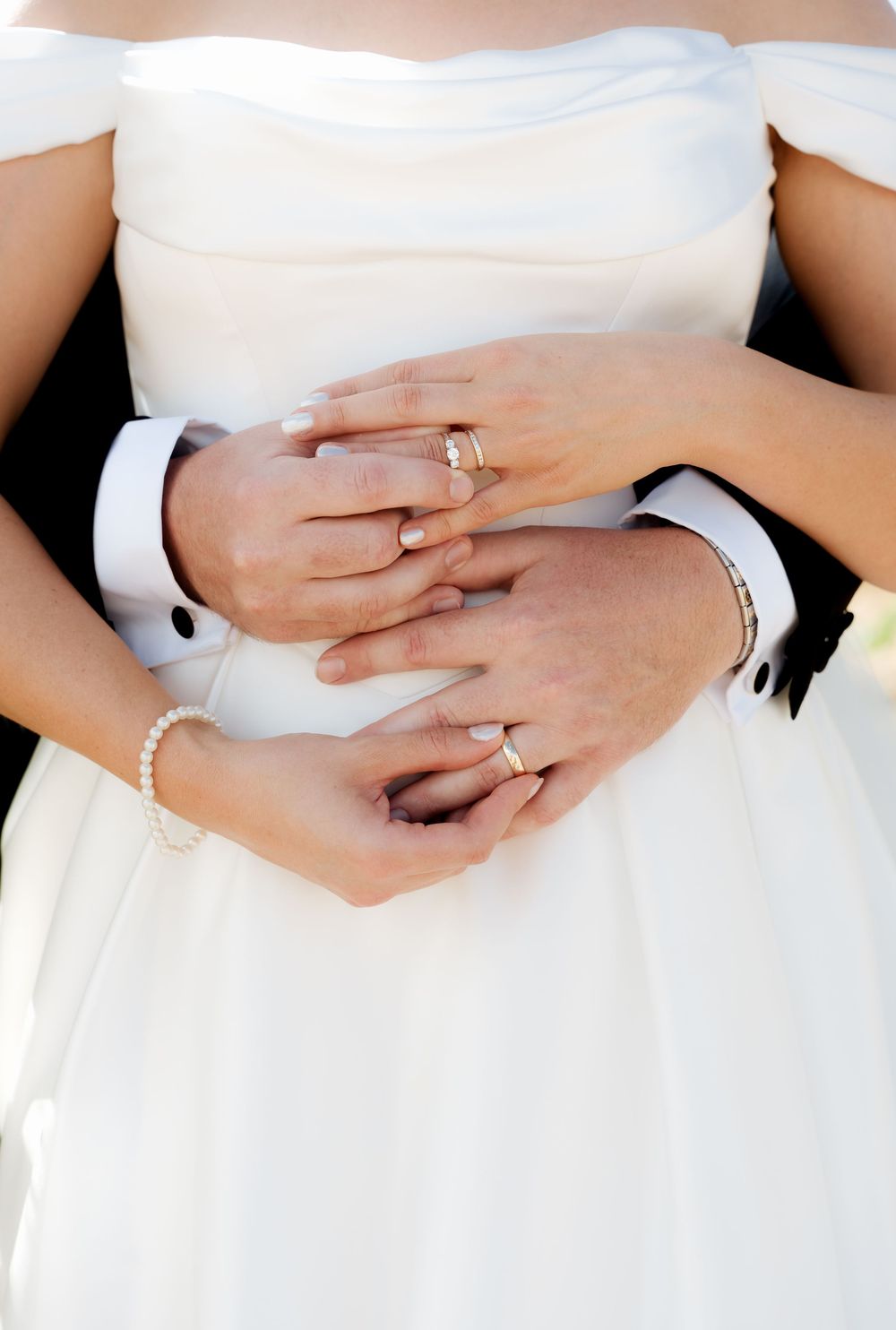 Close-up shots of hands wearing wedding rings against white dress fabric show romantic wedding day details.