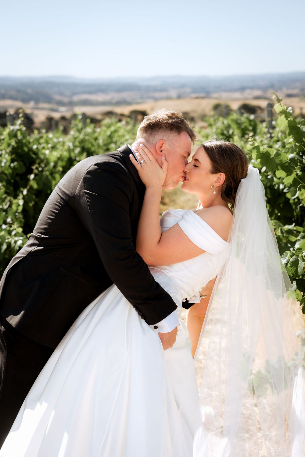 Romantic sequence of newlyweds kissing in a scenic vineyard with rolling hills in the background.