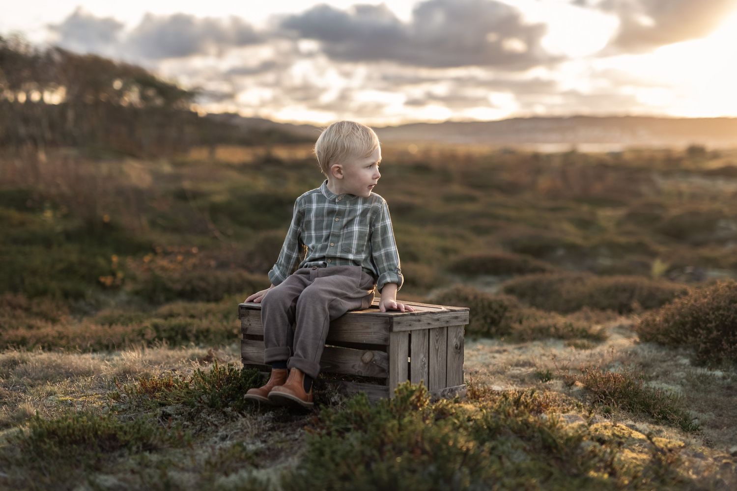 Pojke sitter på trälåda. Det är solnedgång i bakgrunden.