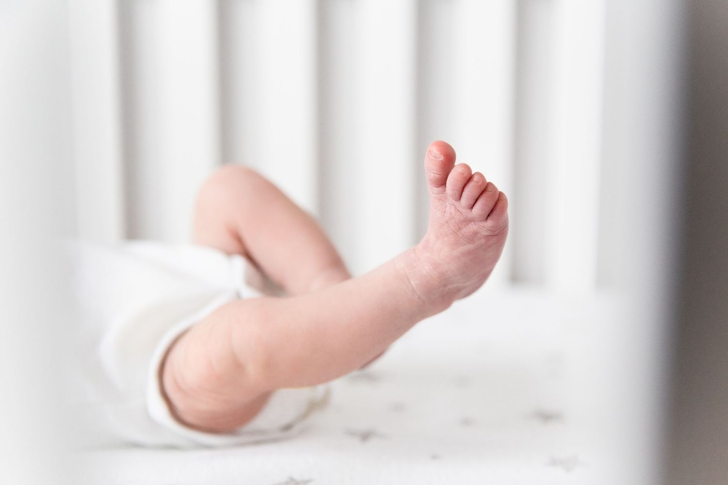 Close-up of newborn wrinkly toes and leg kicking in white crib