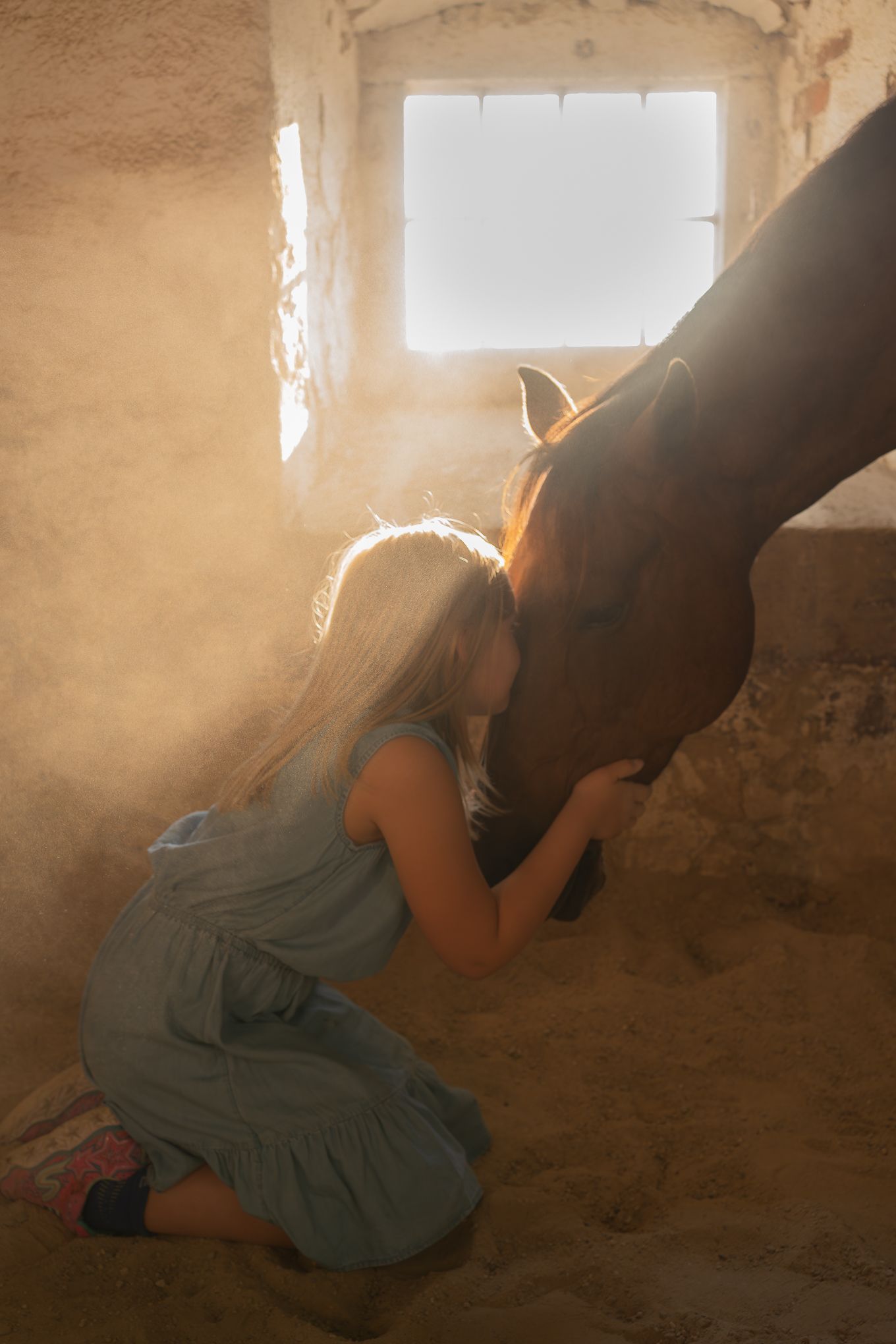 A figure in a blue dress crouches in a sunlit corner of a rustic stone room.