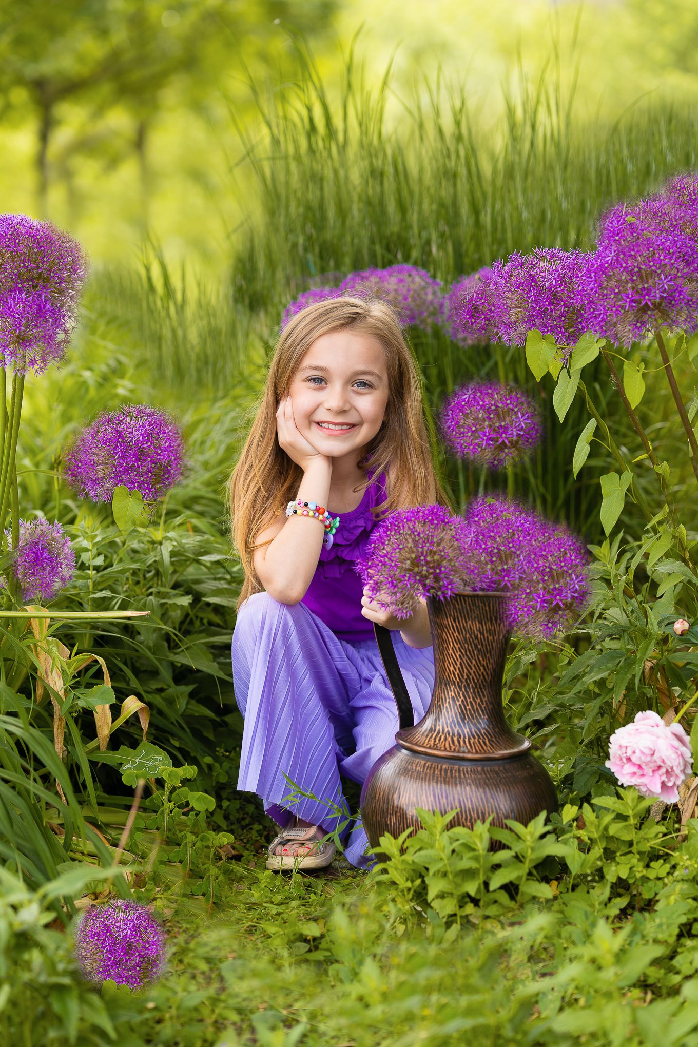 Kinderfotografie - Garden portrait of a girl with bronze vase surrounded by blooming purple allium flowers.
