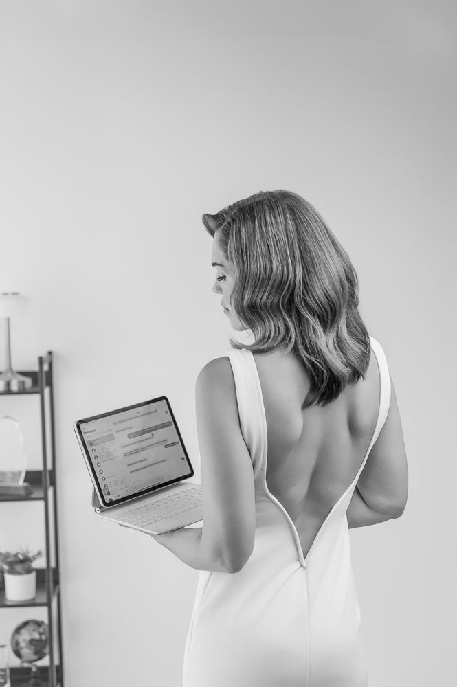 Woman in white tank top looking at mobile device in minimalist room with gray walls.