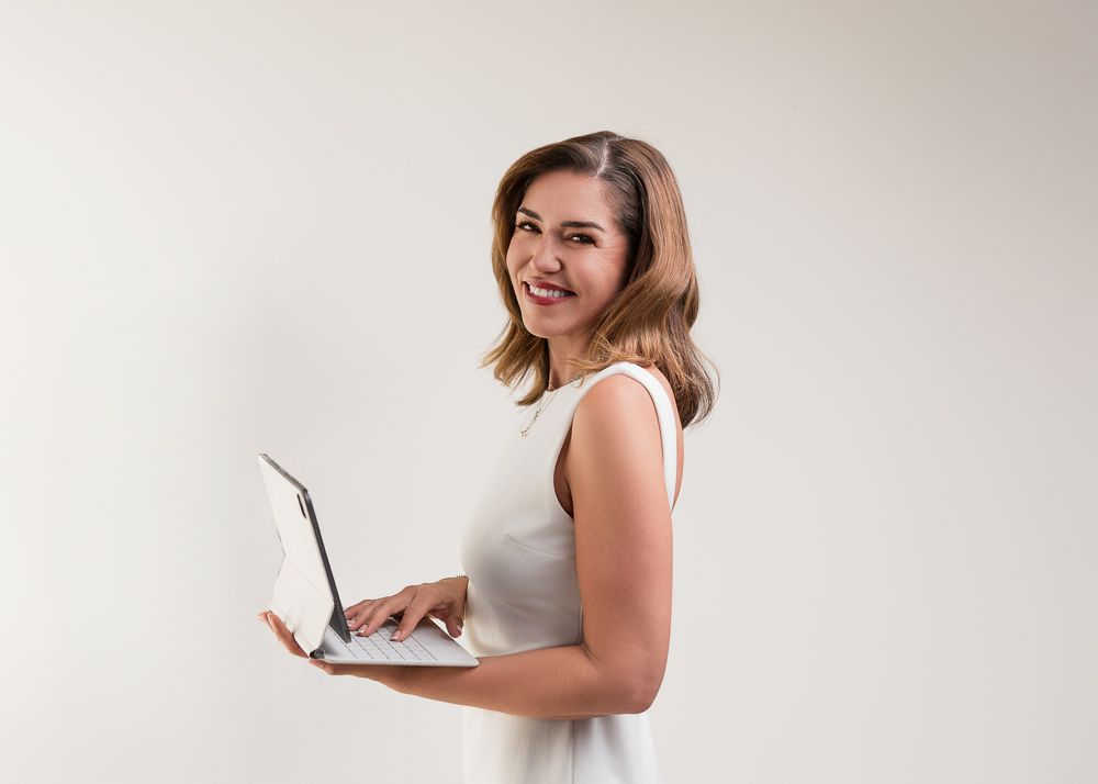 A person in a white sleeveless top poses with a brown mid-century modern armchair in a studio setting.