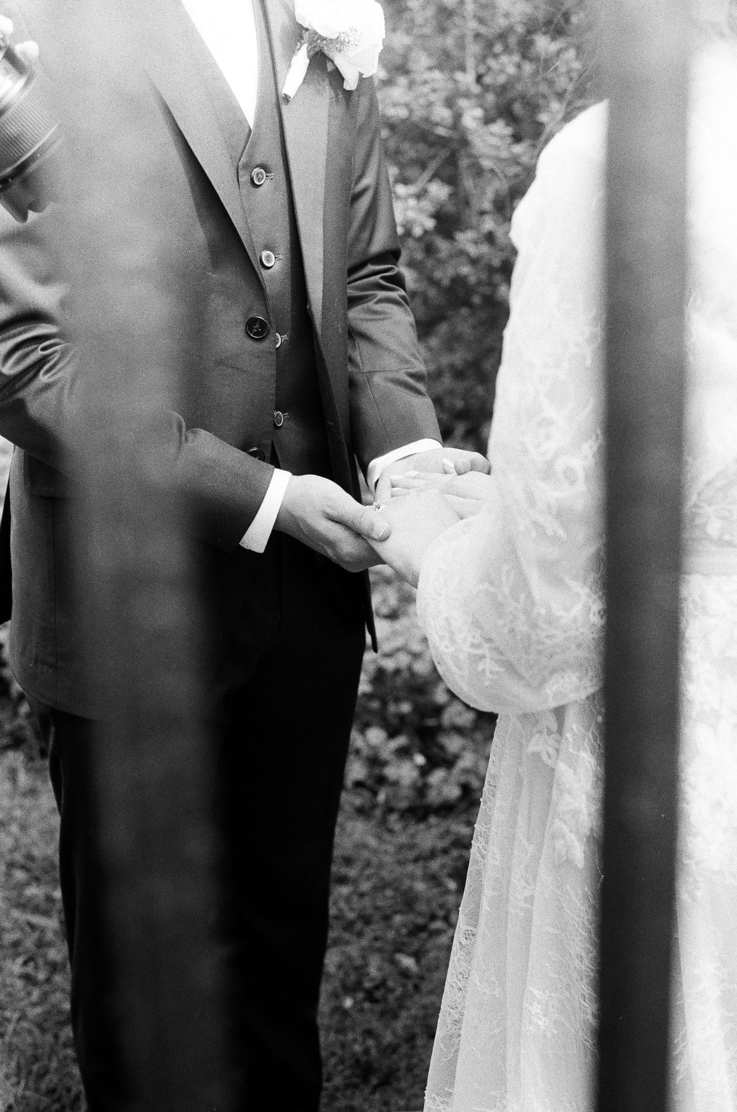 Black and white photo of groom in three-piece suit holding bride's hands during wedding ceremony.