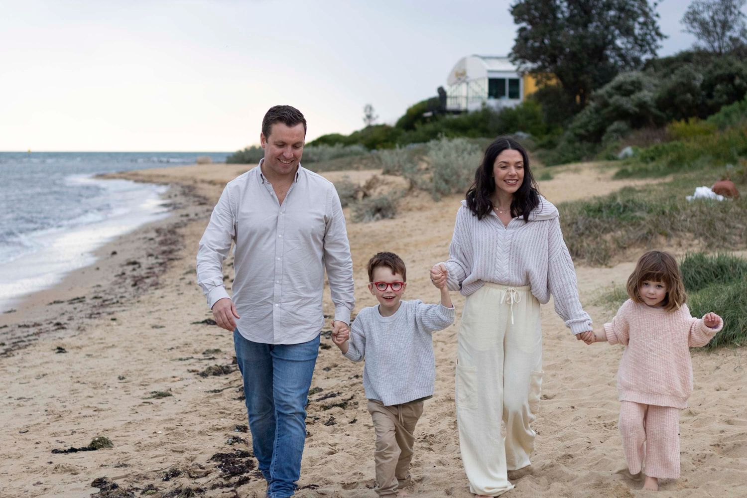 Family of four walking together along the beach at sunset.
