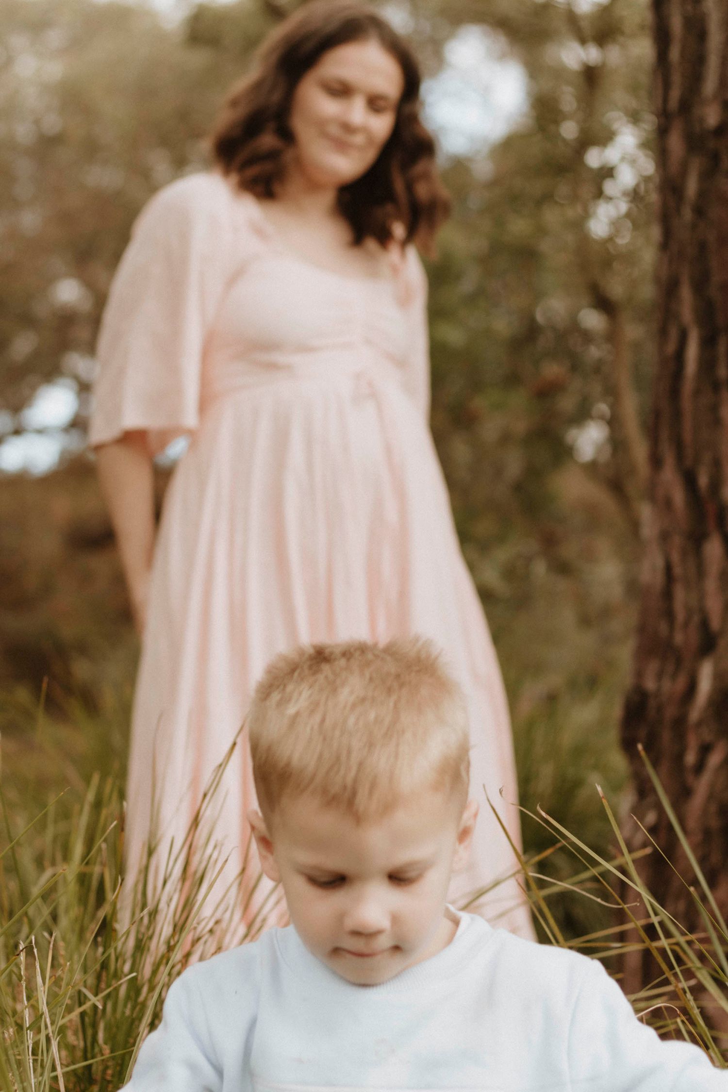 Outdoor family maternity photo in soft pink dress with trees in background.