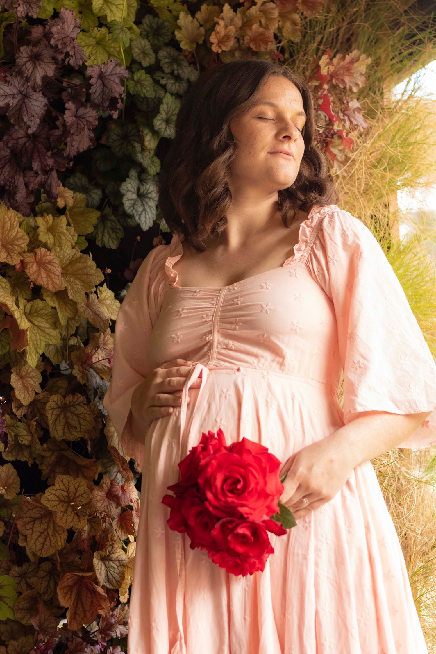 Romantic maternity portrait with red flower accent against floral backdrop.