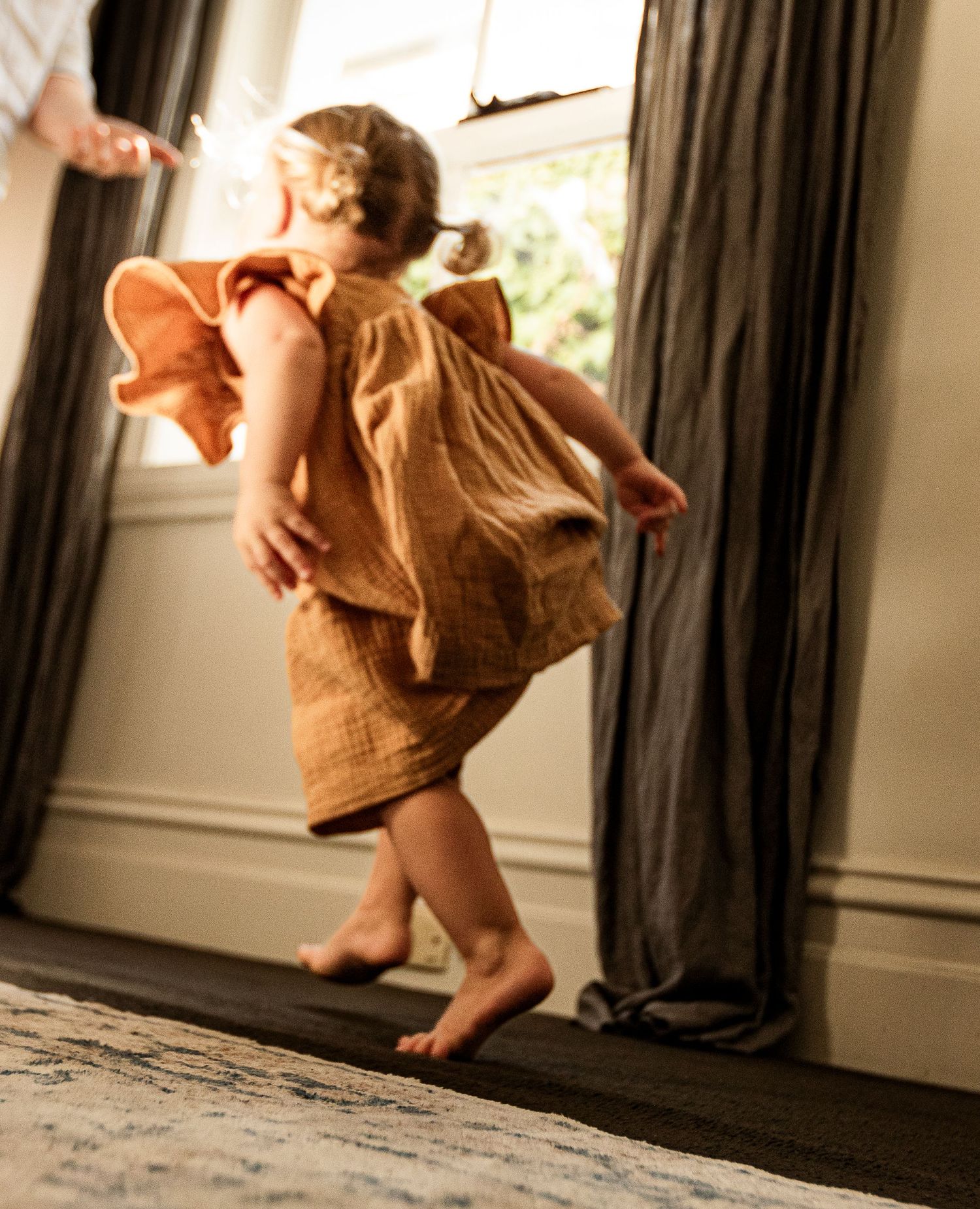 Young child twirling in an orange dress by window with natural lighting.