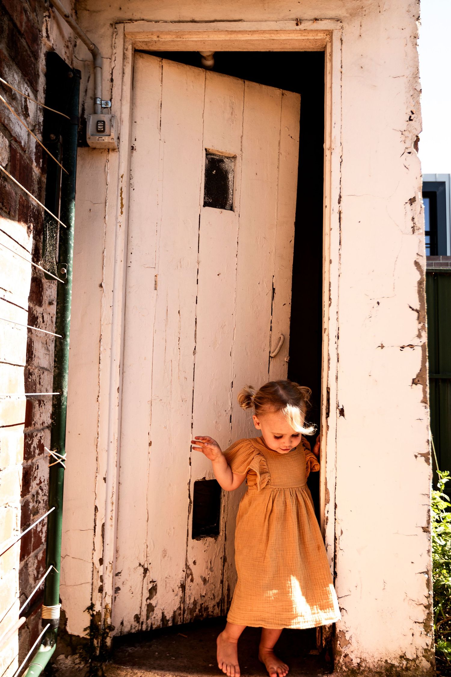 A soft golden dress stands out against a weathered white doorway in a rustic setting.