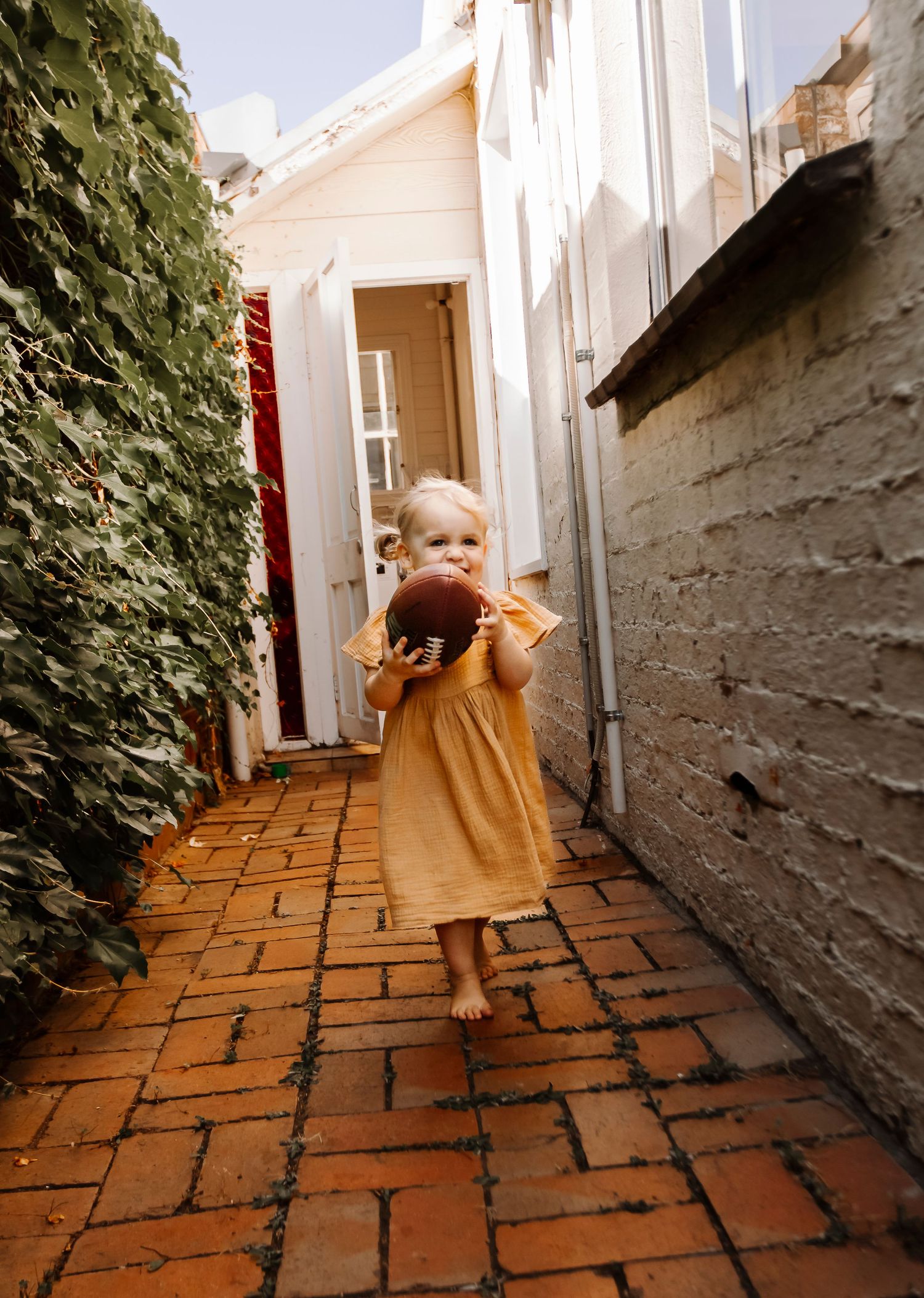 A child in a warm mustard dress runs along a brick path between buildings.