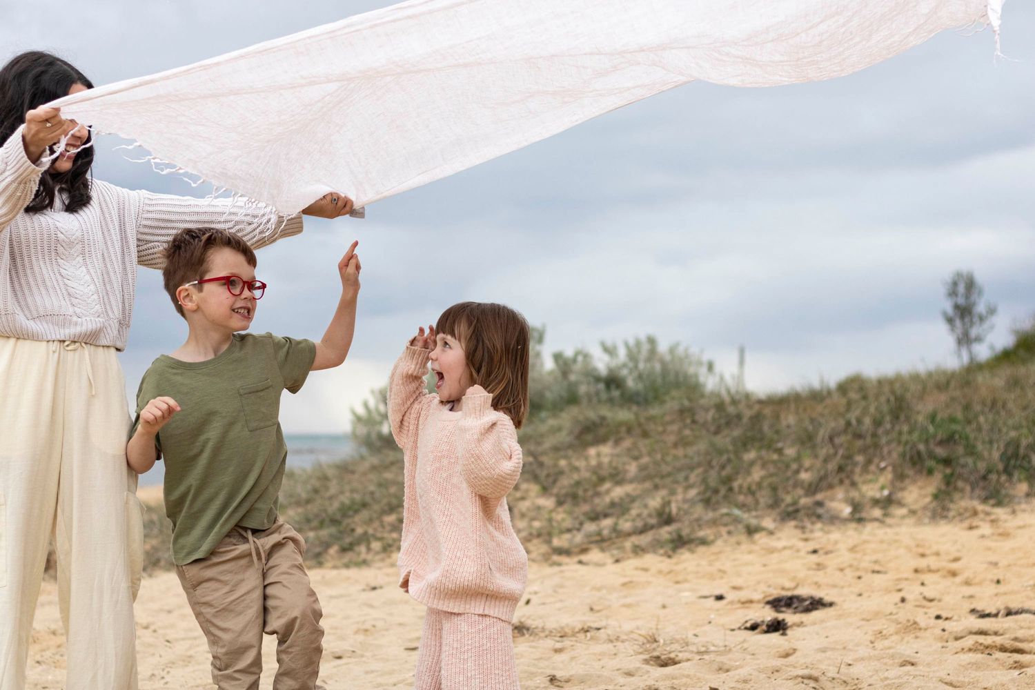A family plays with a white sheet in the wind on a sandy beach.