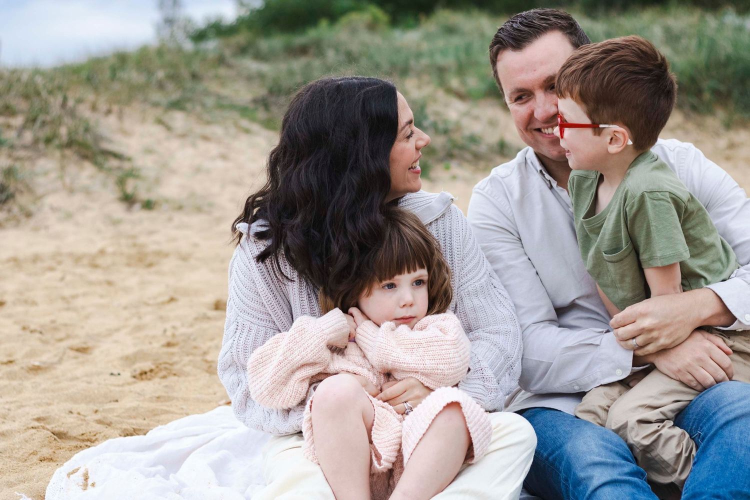 Intimate family moment shared while sitting together on sandy beach.