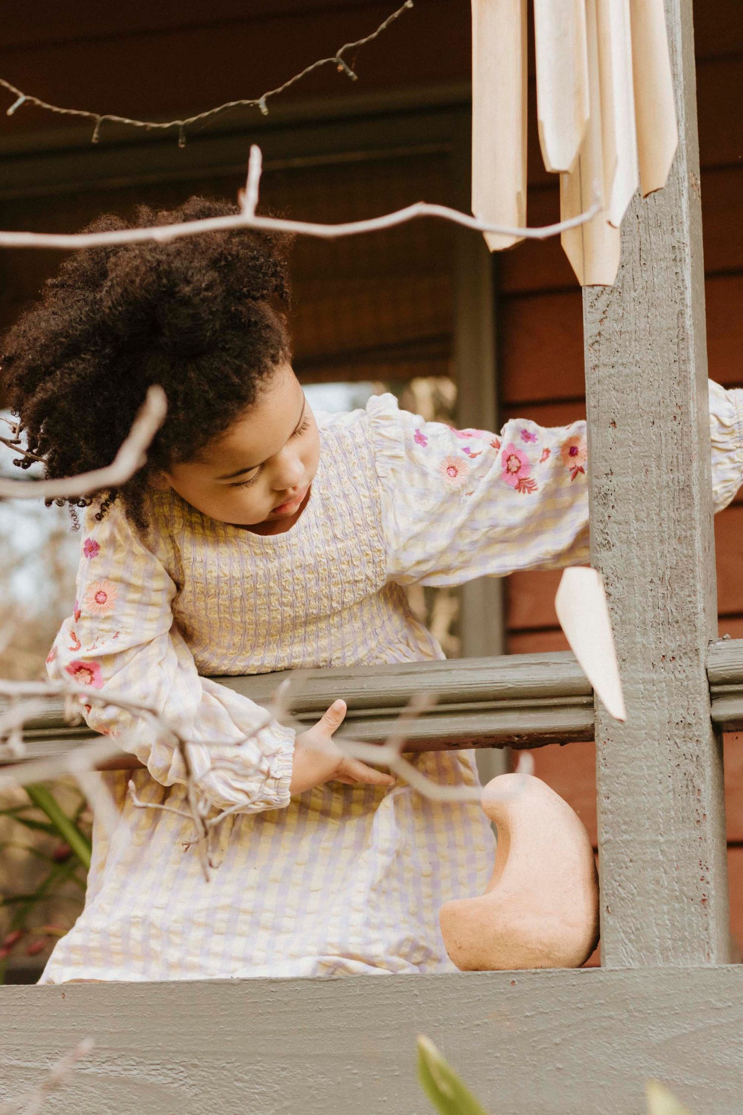 A person in a floral dress leans over a wooden railing under string lights.