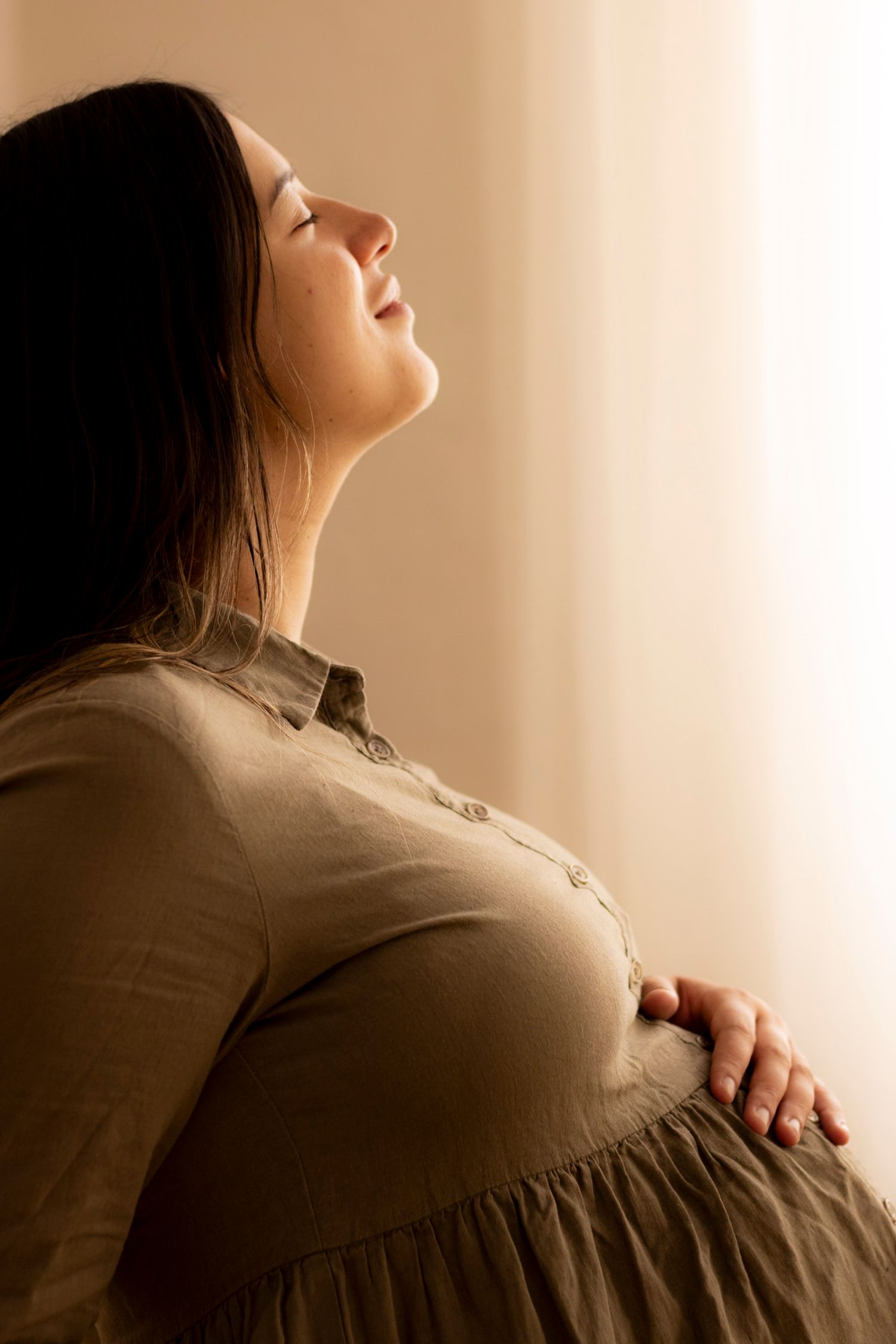 Warm-toned maternity portrait capturing peaceful moment by window.
