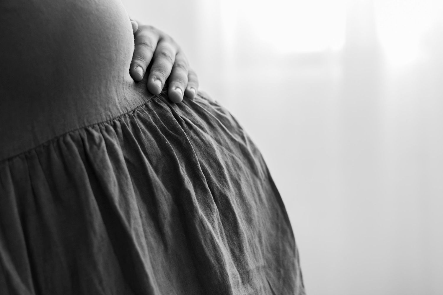 Black and white artistic maternity photo with dramatic side lighting.