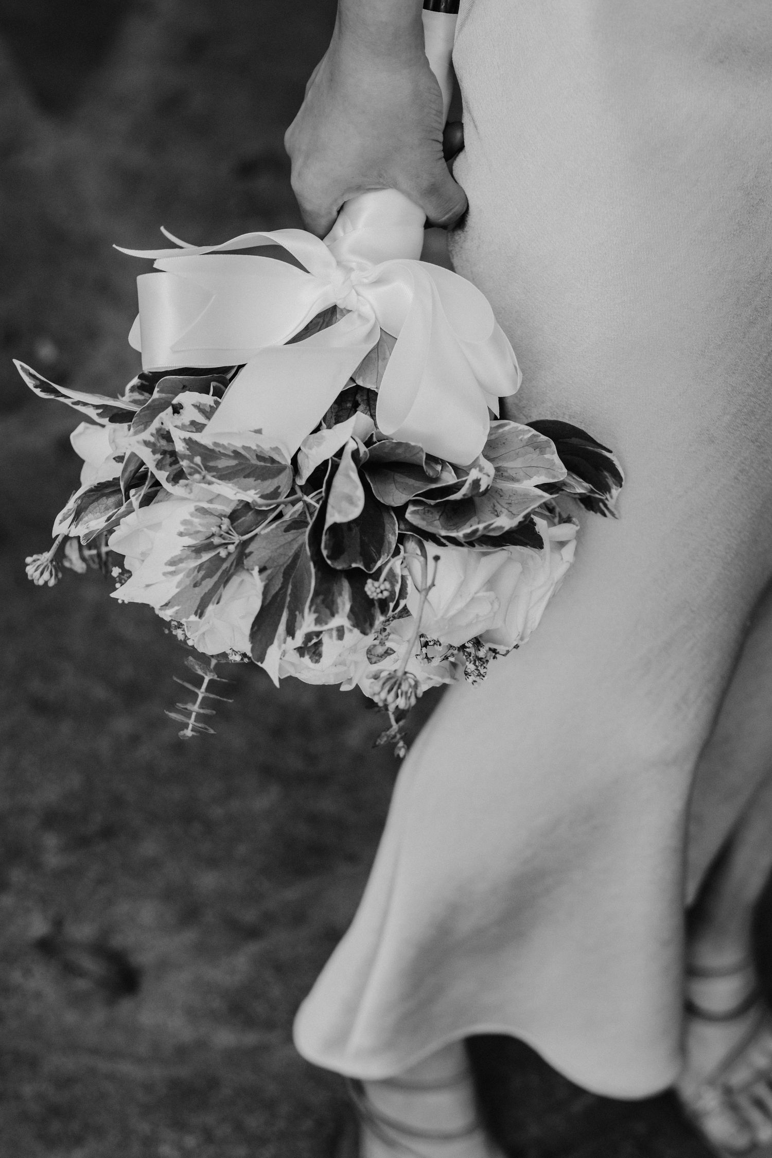 Close-up black and white shot of a white wedding bouquet being held against a dress.