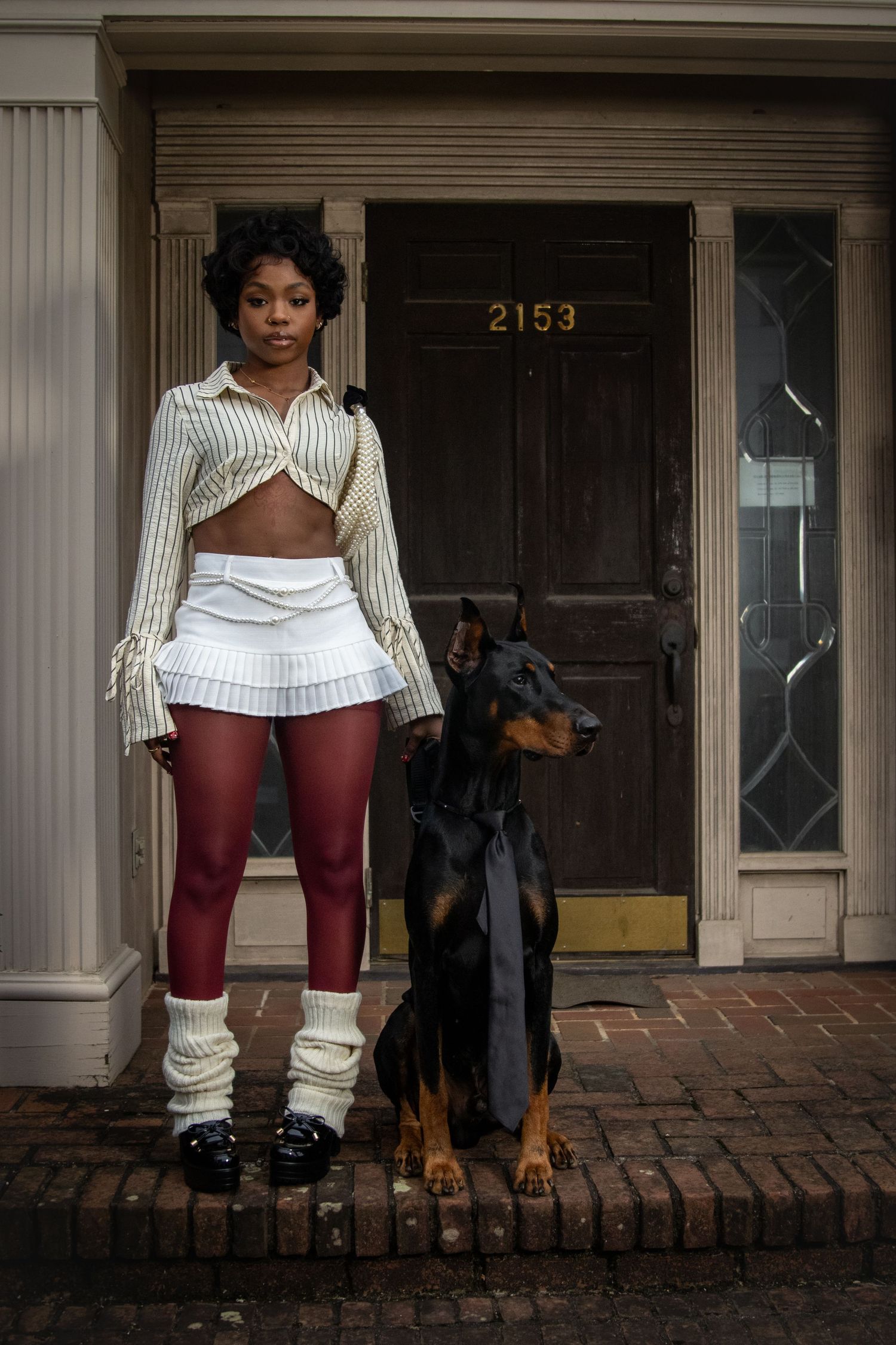 Woman in striped crop top and red leggings standing with a Doberman outside building 2153.