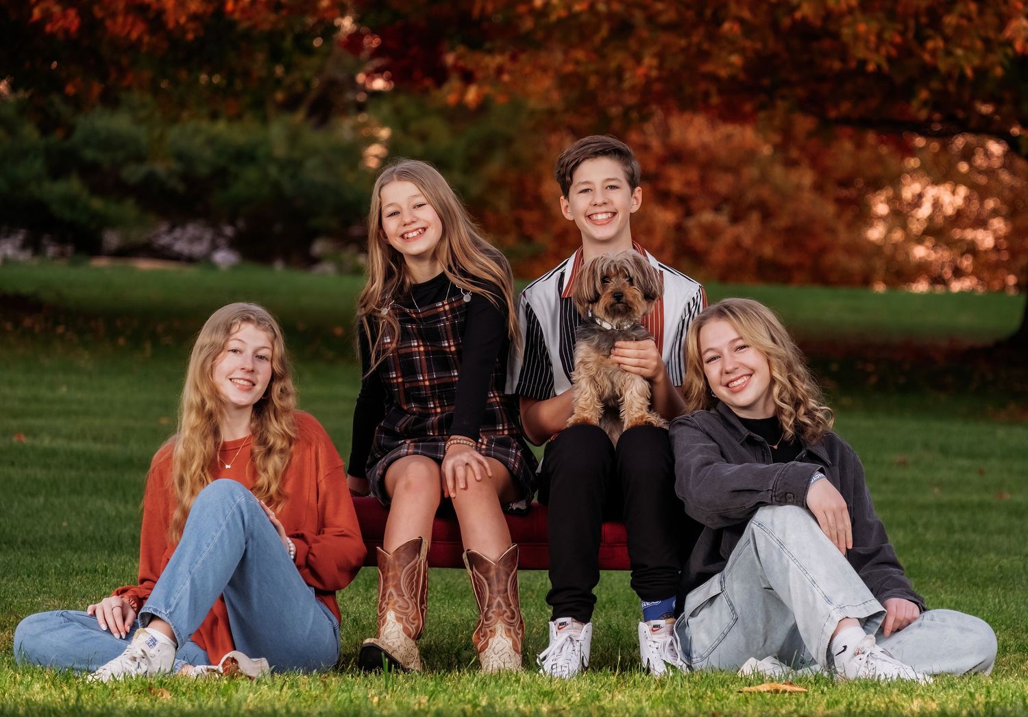 Family portrait featuring six people posed together outdoors with vibrant red fall foliage in the background.