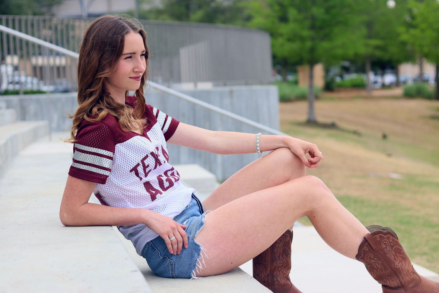 Young woman in a Texas A&M jersey and cowboy boots sitting on steps outdoors.