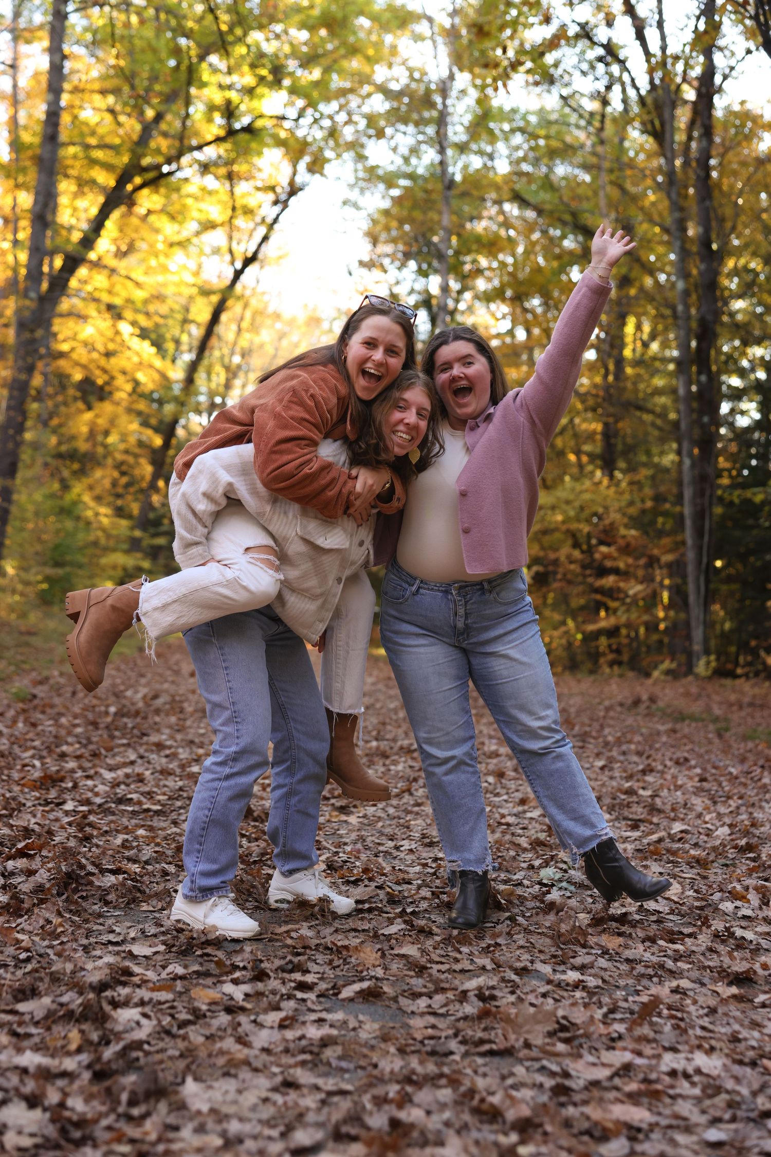 Three joyful young women laughing and posing playfully in a colorful autumn forest.