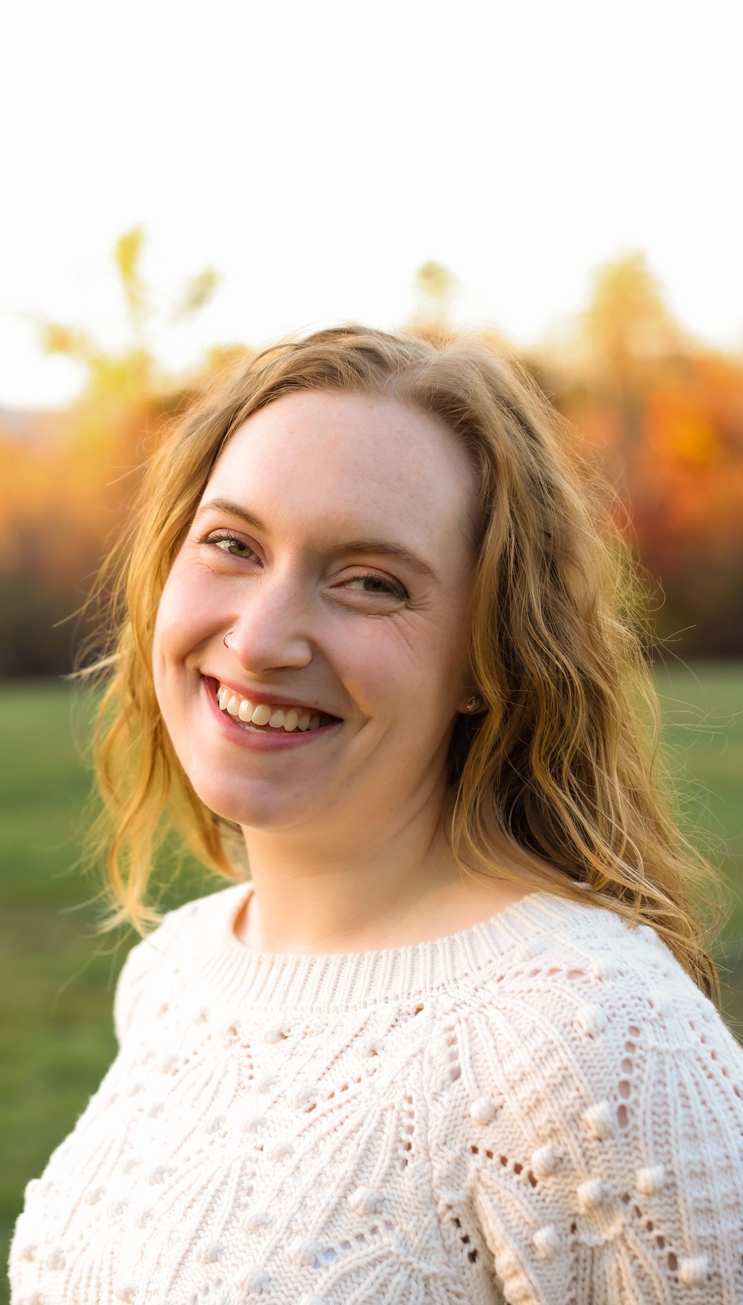 Close-up portrait of a smiling young woman in a white knit sweater in an autumn field.
