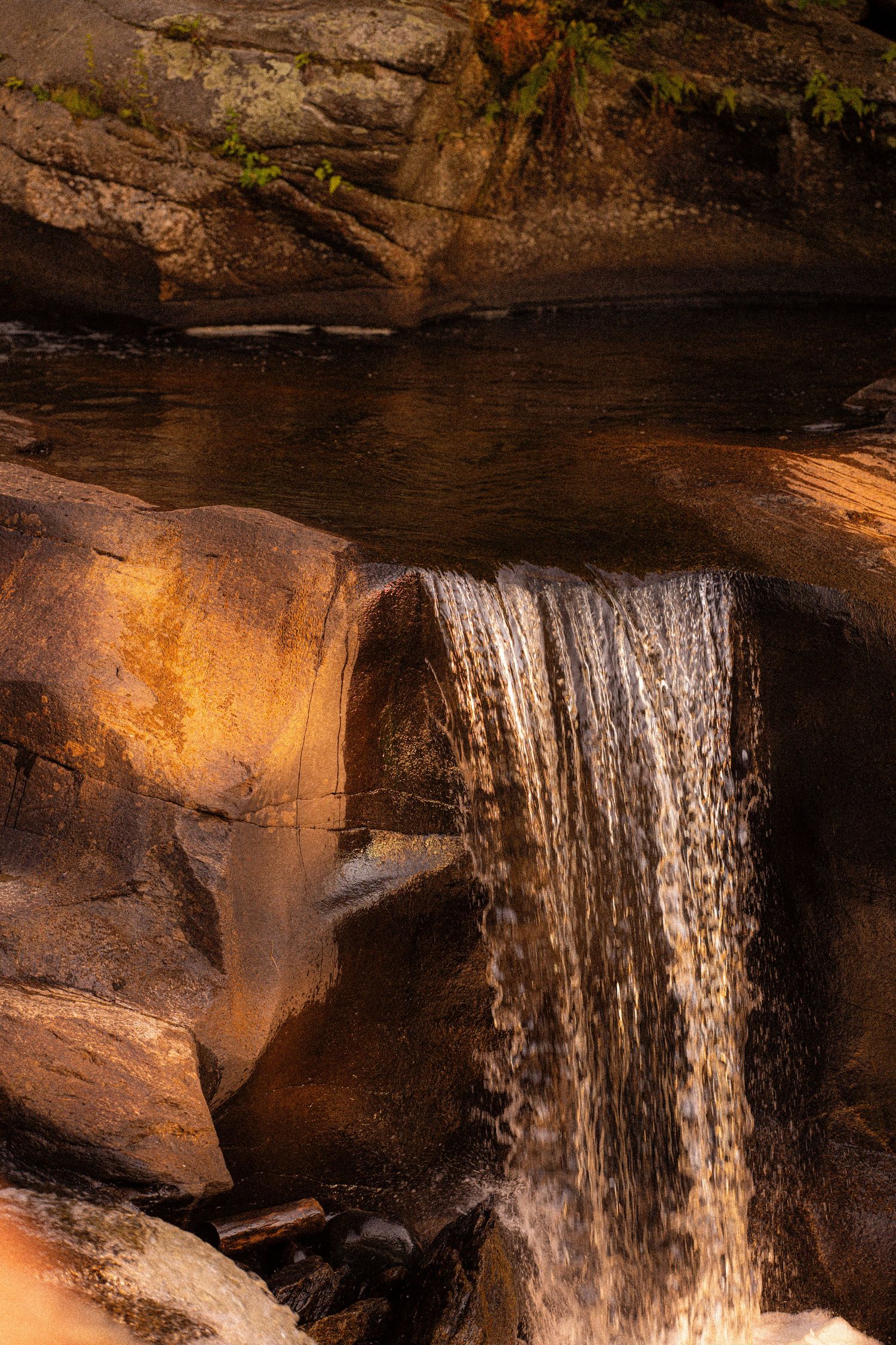 Golden-lit waterfall cascading over smooth rocks into a serene pool, bathed in warm sunset light.